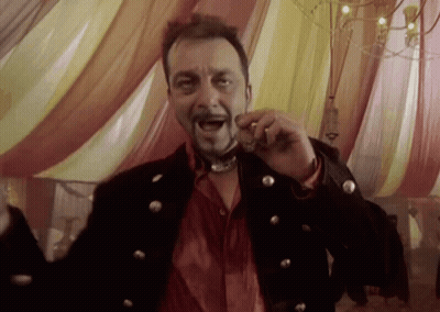 A Man In A Black Jacket And Red Shirt Is Holding Something In His Mouth While Standing In Front Of A Tent GIF