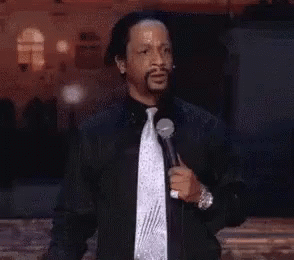 A Man In A Black Jacket And Tie Is Holding A Microphone And Giving A Speech . GIF