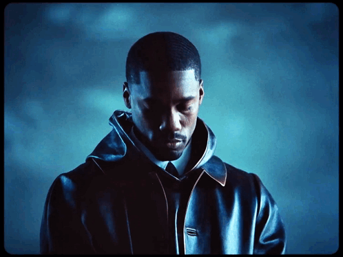 A Man In A Black Jacket And Tie Looks Down At Something GIF