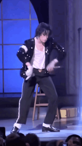A Man In A Black Jacket And White Pants Is Dancing On Stage GIF
