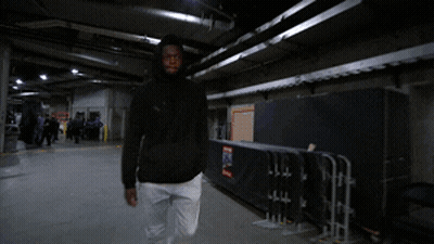 A Man In A Black Jacket And White Pants Is Walking Through A Dark Room GIF