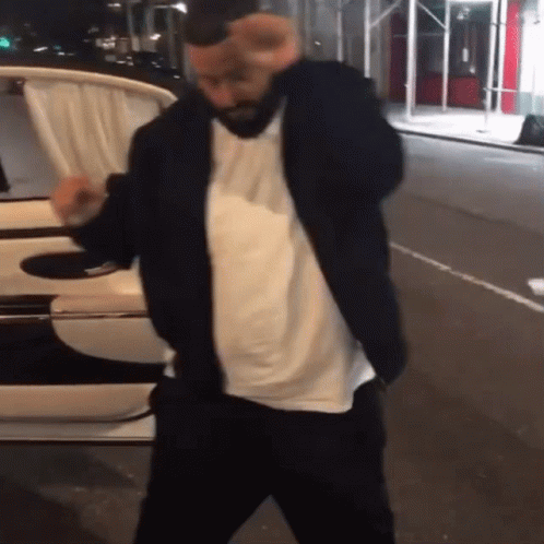 A Man In A Black Jacket And White Shirt Is Dancing On The Street GIF