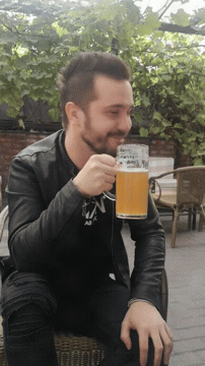 A Man In A Black Jacket Drinks From A Glass With The Letter N On It GIF