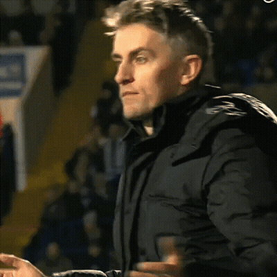 A Man In A Black Jacket Is Clapping His Hands In A Crowd GIF
