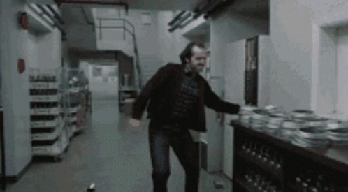 A Man In A Black Jacket Is Dancing In A Dark Hallway GIF