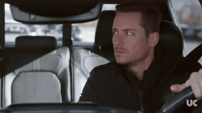 A Man In A Black Jacket Is Driving A Car With The Letters Uc On The Steering Wheel GIF