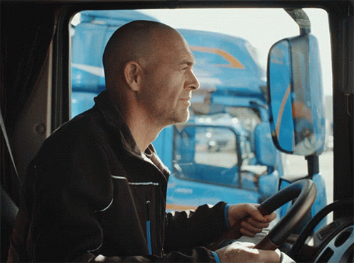 A Man In A Black Jacket Is Driving A Truck GIF