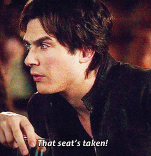 A Man In A Black Jacket Is Holding A Glass And Says That Seat 'S Taken GIF