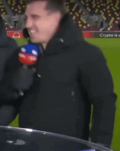 A Man In A Black Jacket Is Holding A Microphone In Front Of A Soccer Field That Has The Word Qatar On It GIF