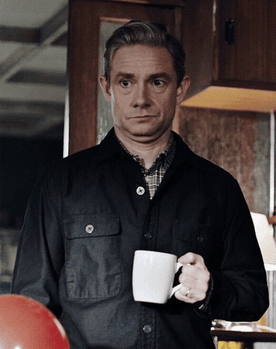 A Man In A Black Jacket Is Holding A White Coffee Cup GIF