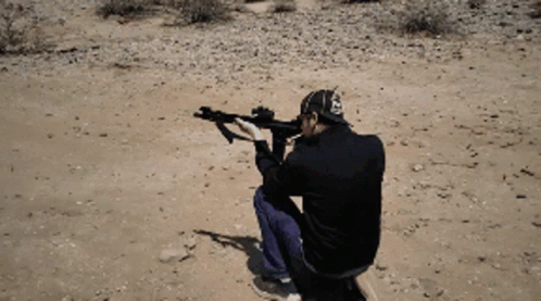A Man In A Black Jacket Is Kneeling Down Holding A Gun GIF