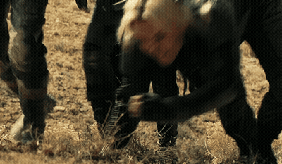 A Man In A Black Jacket Is Kneeling Down In The Dirt With A Knife In His Hand GIF