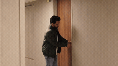 A Man In A Black Jacket Is Opening A Door In A Hallway GIF