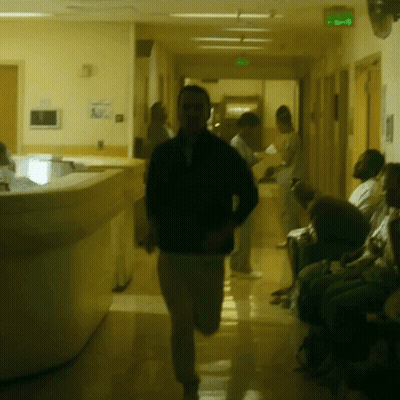 A Man In A Black Jacket Is Running Down A Hallway GIF