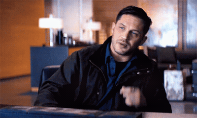 A Man In A Black Jacket Is Sitting At A Table Talking GIF