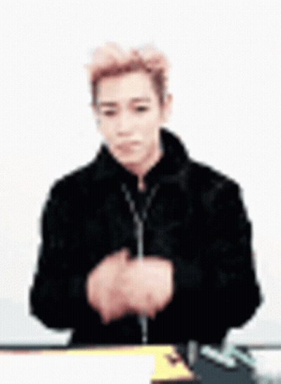 A Man In A Black Jacket Is Sitting At A Table With His Hands Folded In Front Of Him . GIF