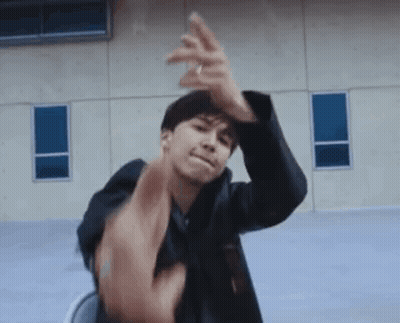 A Man In A Black Jacket Is Sitting In A Chair And Making A Funny Face With His Hands . GIF
