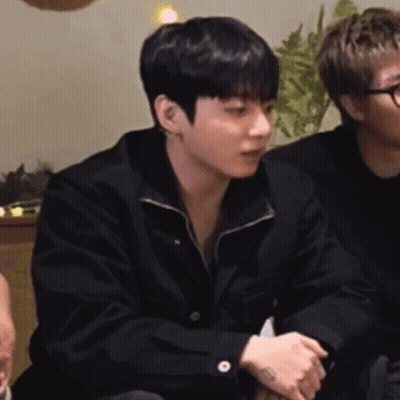 A Man In A Black Jacket Is Sitting Next To Another Man In A Black Shirt . GIF