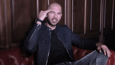 A Man In A Black Jacket Is Sitting On A Red Leather Couch With His Arms Outstretched GIF