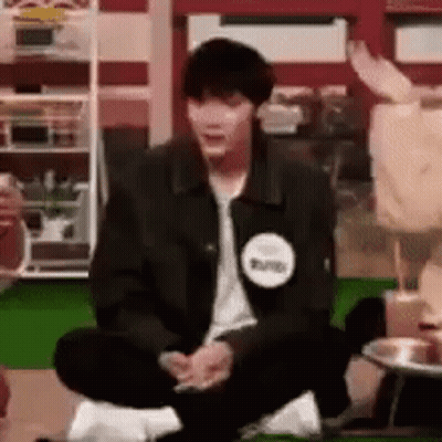 A Man In A Black Jacket Is Sitting On The Floor With His Legs Crossed In A Room . GIF