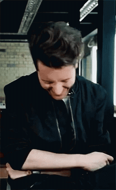 A Man In A Black Jacket Is Smiling And Looking Down GIF