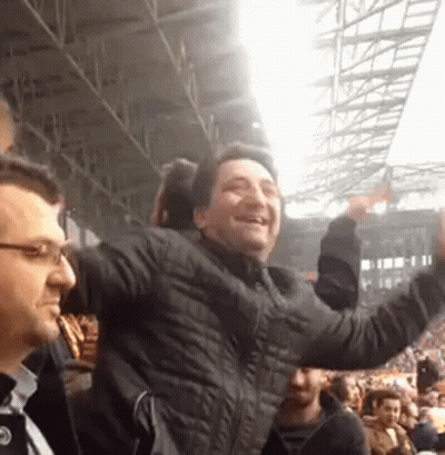 A Man In A Black Jacket Is Standing In A Crowd Of People . GIF