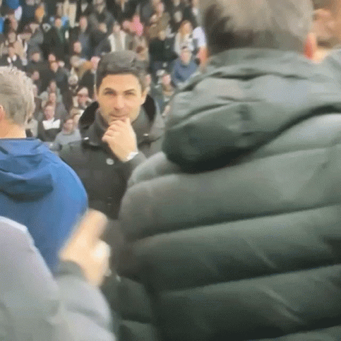 A Man In A Black Jacket Is Standing In A Crowd Of People GIF
