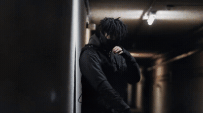 A Man In A Black Jacket Is Standing In A Dark Room GIF
