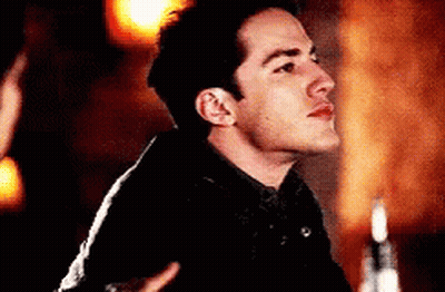 A Man In A Black Jacket Is Standing In A Dark Room . GIF