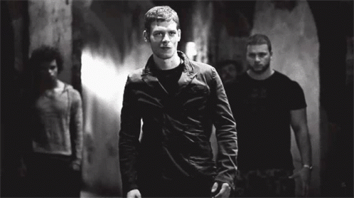 A Man In A Black Jacket Is Standing In A Dark Room GIF