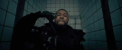 A Man In A Black Jacket Is Standing In Front Of A Blue Tiled Wall GIF