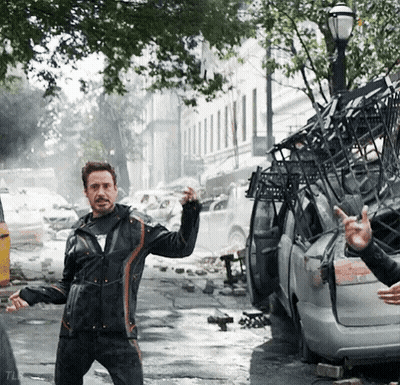A Man In A Black Jacket Is Standing In Front Of A Destroyed Car And Giving The Middle Finger GIF