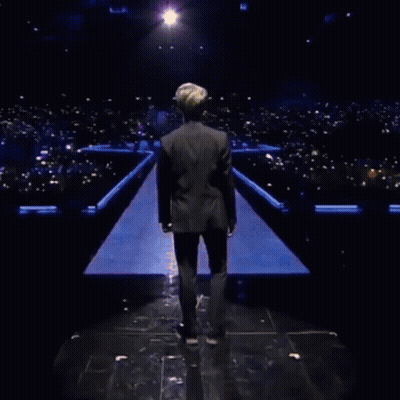 A Man In A Black Jacket Is Standing In Front Of A Field Of Skulls GIF