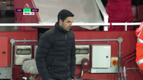 A Man In A Black Jacket Is Standing In Front Of A Scoreboard That Says Ars 2-1 Wol GIF