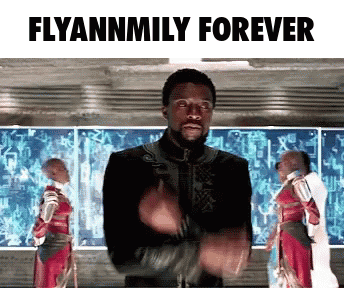 A Man In A Black Jacket Is Standing In Front Of A Screen That Says Flyannmily Forever GIF