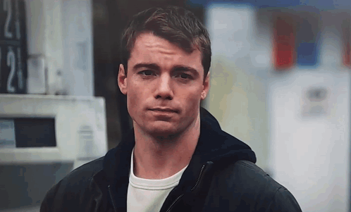A Man In A Black Jacket Is Standing In Front Of A Sign That Says 21 . GIF