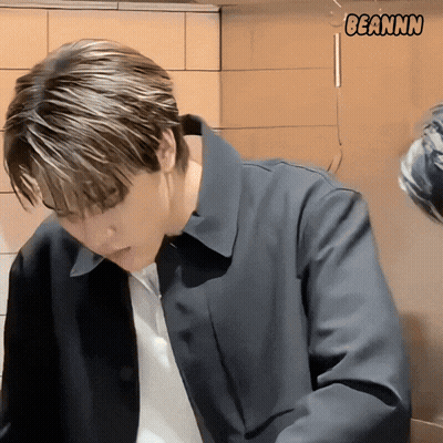 A Man In A Black Jacket Is Standing In Front Of A Wall With Beannn Written On It GIF