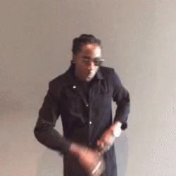 A Man In A Black Jacket Is Standing In Front Of A White Wall . GIF