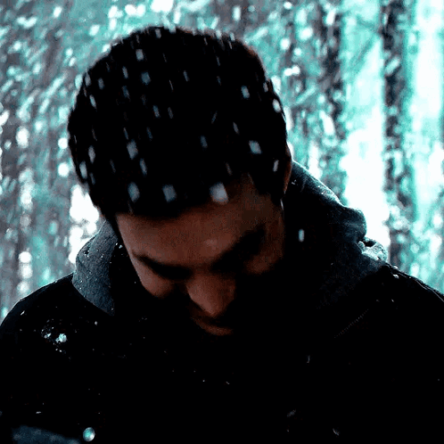 A Man In A Black Jacket Is Standing In The Snow With Snow Falling On His Head . GIF