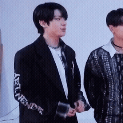 A Man In A Black Jacket Is Standing Next To Another Man In A Black Shirt . GIF