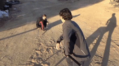 A Man In A Black Jacket Is Standing On A Dirt Road Next To Another Man GIF