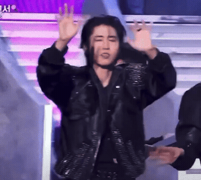 A Man In A Black Jacket Is Standing On A Stage With His Arms Outstretched . GIF