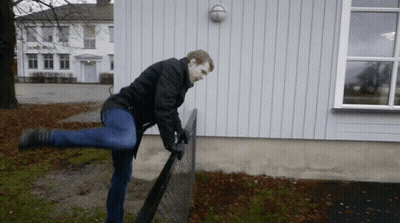 A Man In A Black Jacket Is Standing On One Leg On A Chain Link Fence GIF