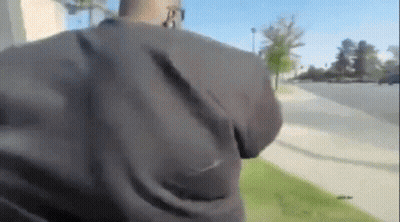 A Man In A Black Jacket Is Walking Down A Sidewalk While Talking On A Cell Phone . GIF