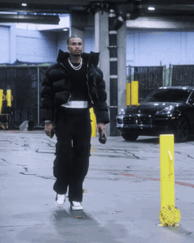 A Man In A Black Jacket Is Walking Down A Street GIF