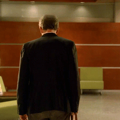 A Man In A Black Jacket Is Walking In A Room GIF