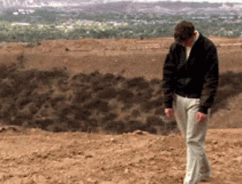 A Man In A Black Jacket Is Walking On A Dirt Hill GIF