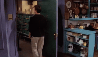 A Man In A Black Jacket Is Walking Through A Doorway GIF