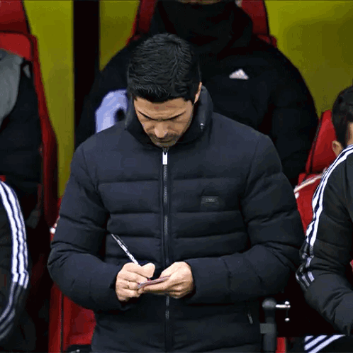 A Man In A Black Jacket Is Writing On His Phone GIF