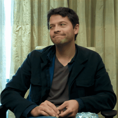 A Man In A Black Jacket Sits In A Chair With His Hands Folded GIF